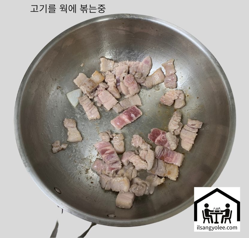 스테인리스 웍 에 식용유를 두르고 깍둑썰기한 돼지고기들을 넣고 볶고 있는 모습.